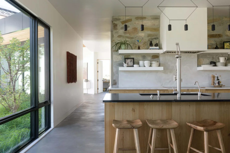 The kitchen features a Venetian plaster hood and quartzite countertops surrounded by hardware-free, white oak, wire-brushed cabinets. Black steel uppers with glass doors add contrast. Additional layers include brushed nickel hardware, Wireflow 2D pendant lights. To achieve the look of an old stone wall that had been uncovered, Maren picked up a trowel and worked with the stonemasons to hand-select each stone. The continuous wall wraps to the pantry.