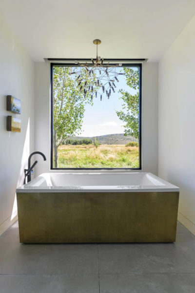 A custom-made chandelier by light artist Robert Townsend illuminates the brass-wrapped Kohler drop-in tub in the spacious primary bathroom.